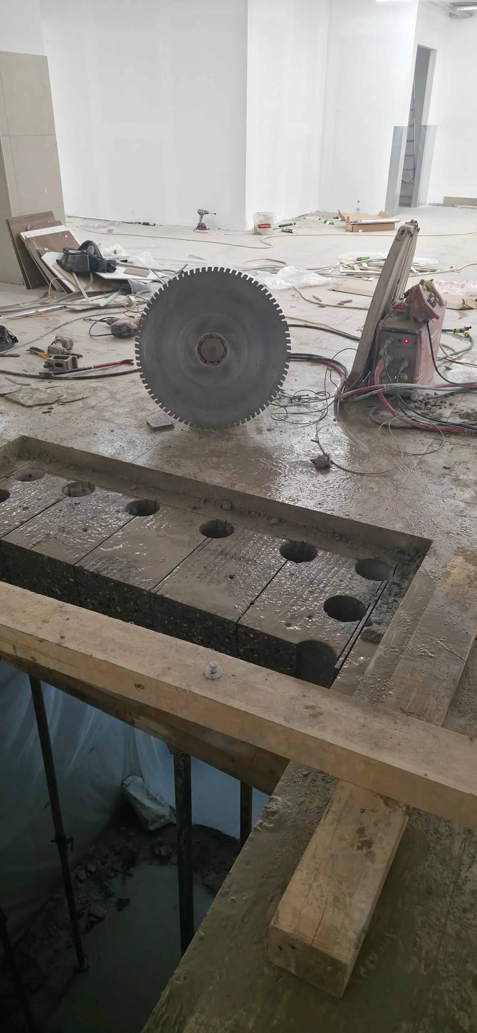 Large saw-cut concrete block rigged to crane straps above a foundation wall