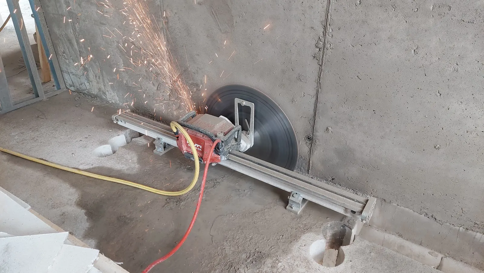 Track-mounted wall saw cutting a reinforced concrete wall, sparks coming off embedded rebar