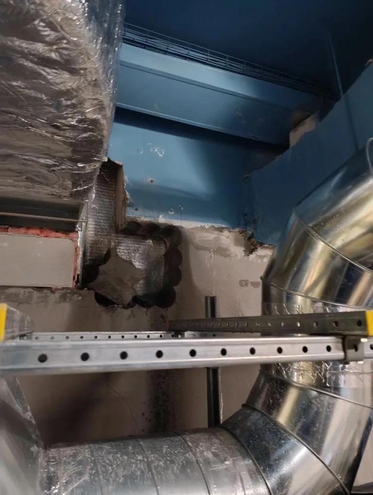 Stitch-drilled rectangular duct opening through a concrete wall next to installed round ductwork
