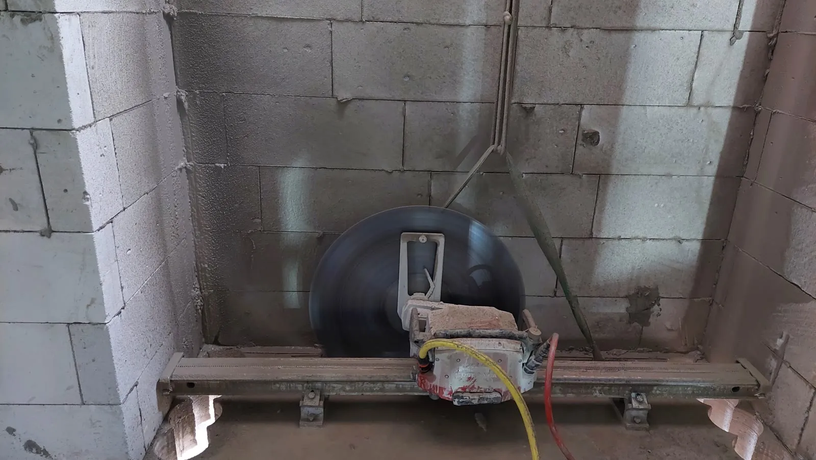 Wall saw blade mid-cut on its track, with core-drilled corner holes visible at the cut line